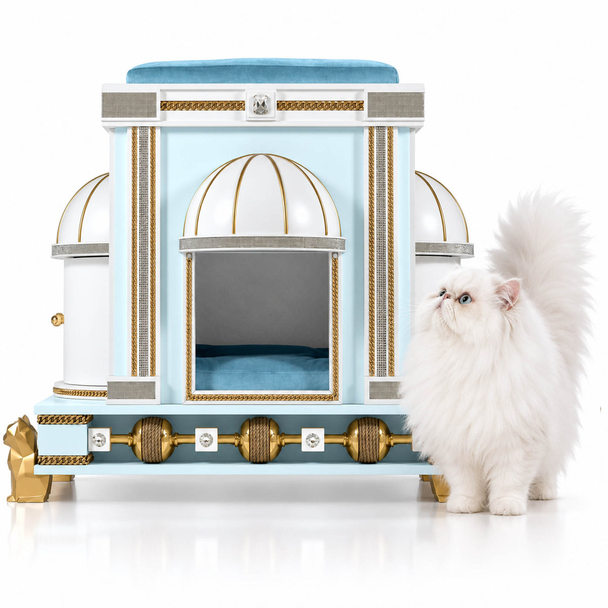 A fluffy white long-haired cat stands beside an ornate light blue and white cat bed with gold trim and dome-shaped openings, photographed on a clean white studio background.