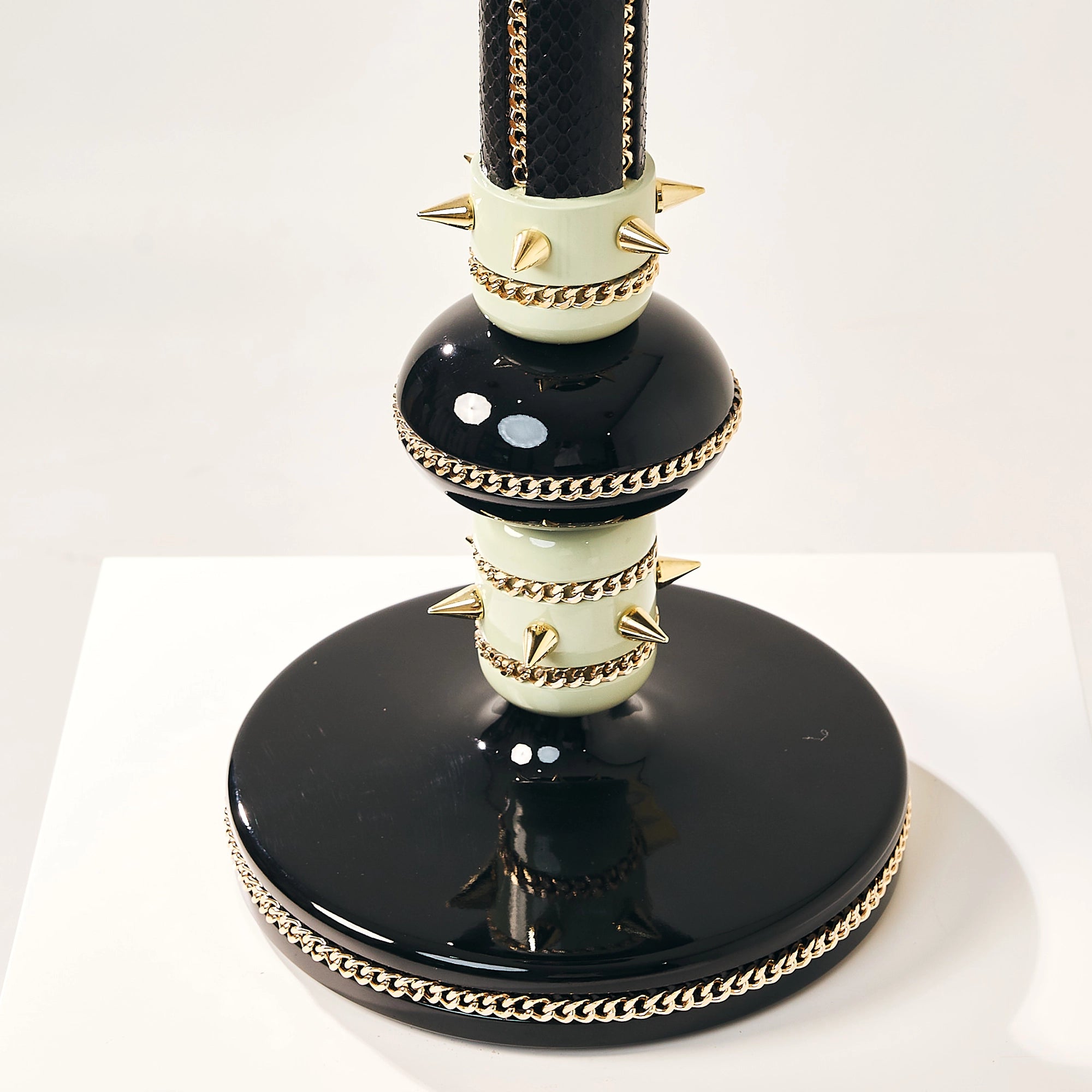 Detail of the dual gold spiked collars above a glossy black circular falcon base.