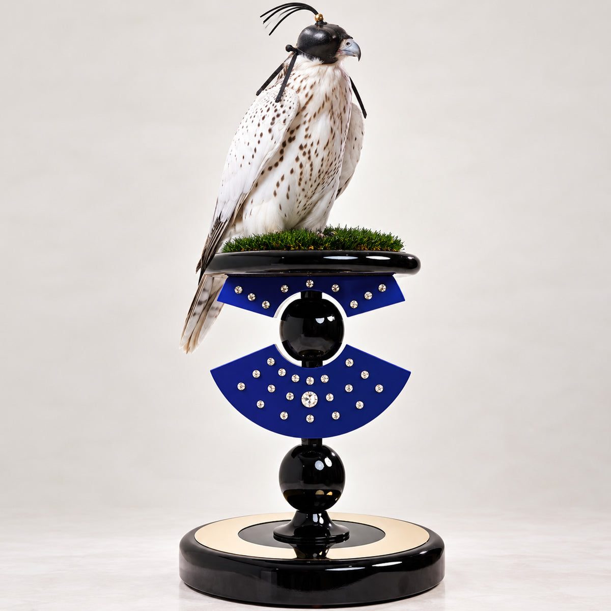 ATTYLAR, The Babylonian Queen Falcon Perch by FUROAR, featuring a sculptural Klein blue and black design with crystal detailing, green grip grass and a white hooded falcon.