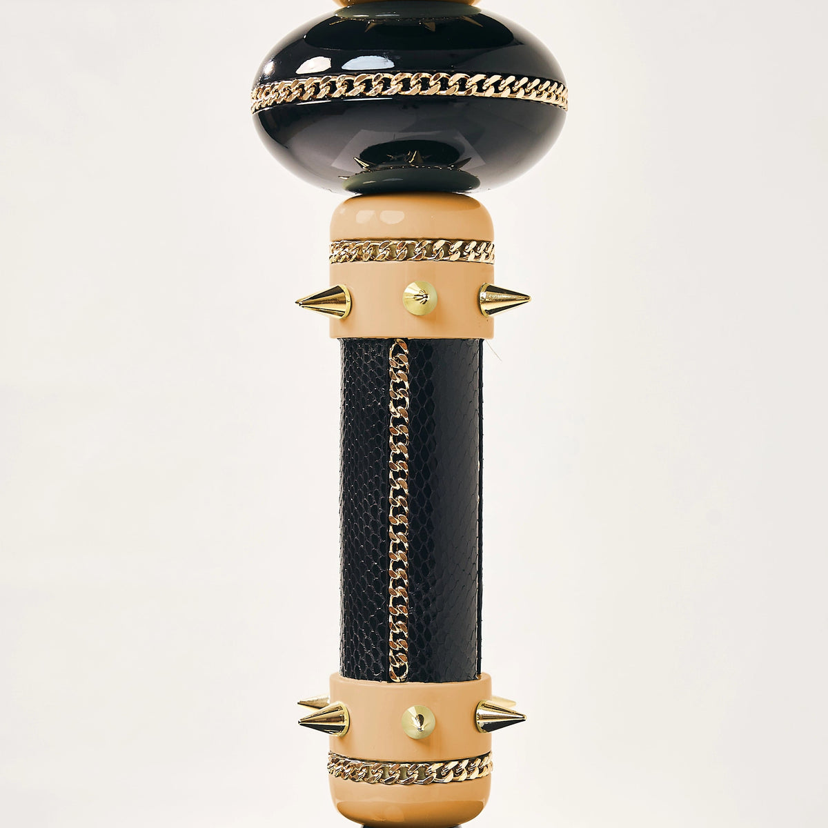 A gothic-style table lamp with a glossy black base and column, accented with gold-tone chains, spikes, and beige wood-like rings, set against a plain white background.
