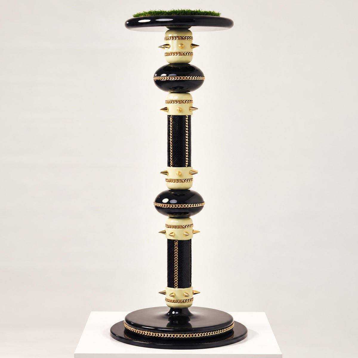 The Crowned Pedestal Falcon Perch by FUROAR, featuring a sculptural black and ivory design with polished gold chain detailing, gold accents and a grass-topped falcon platform.