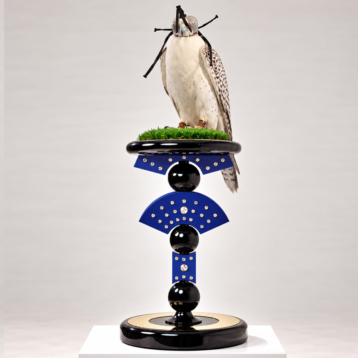 SULTANAR, The Apex Falcon Perch by FUROAR, featuring a sculptural royal blue and black design with crystal detailing, green grip grass and a white hooded falcon.