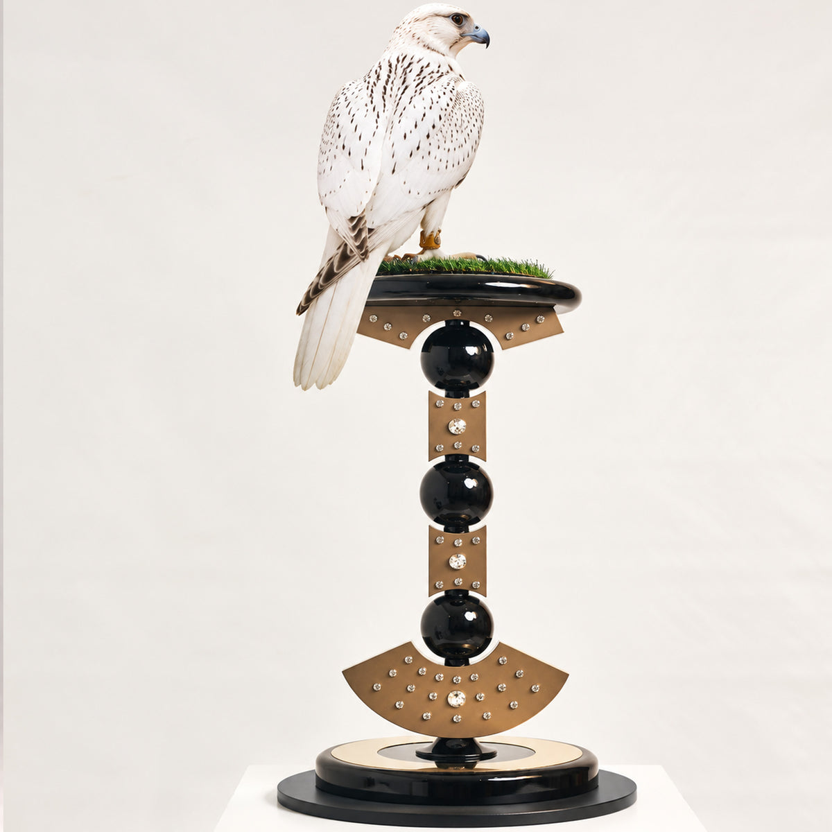 White falcon perched on the FUROAR Tsarina Imperial Falcon Perch, featuring sculptural bronze-gold panels, crystal detailing, glossy black spheres and a circular black-and-gold base.