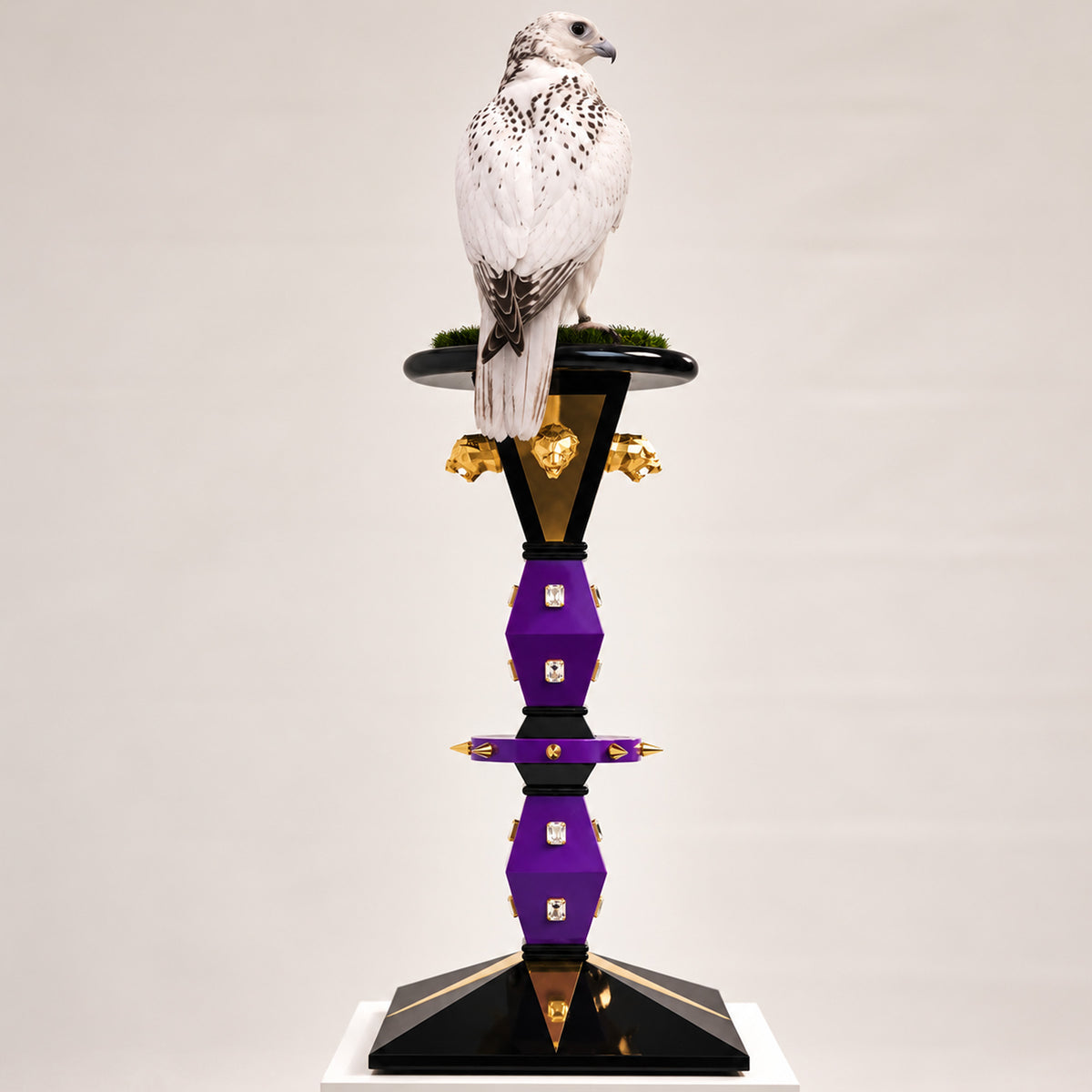 VANDOR | The Imperial Flagship Falcon Perch by FUROAR®, featuring a white speckled falcon on a sculptural purple, black and gold luxury falcon stand with crystal detailing, gold lion motifs and a grass-topped perch.