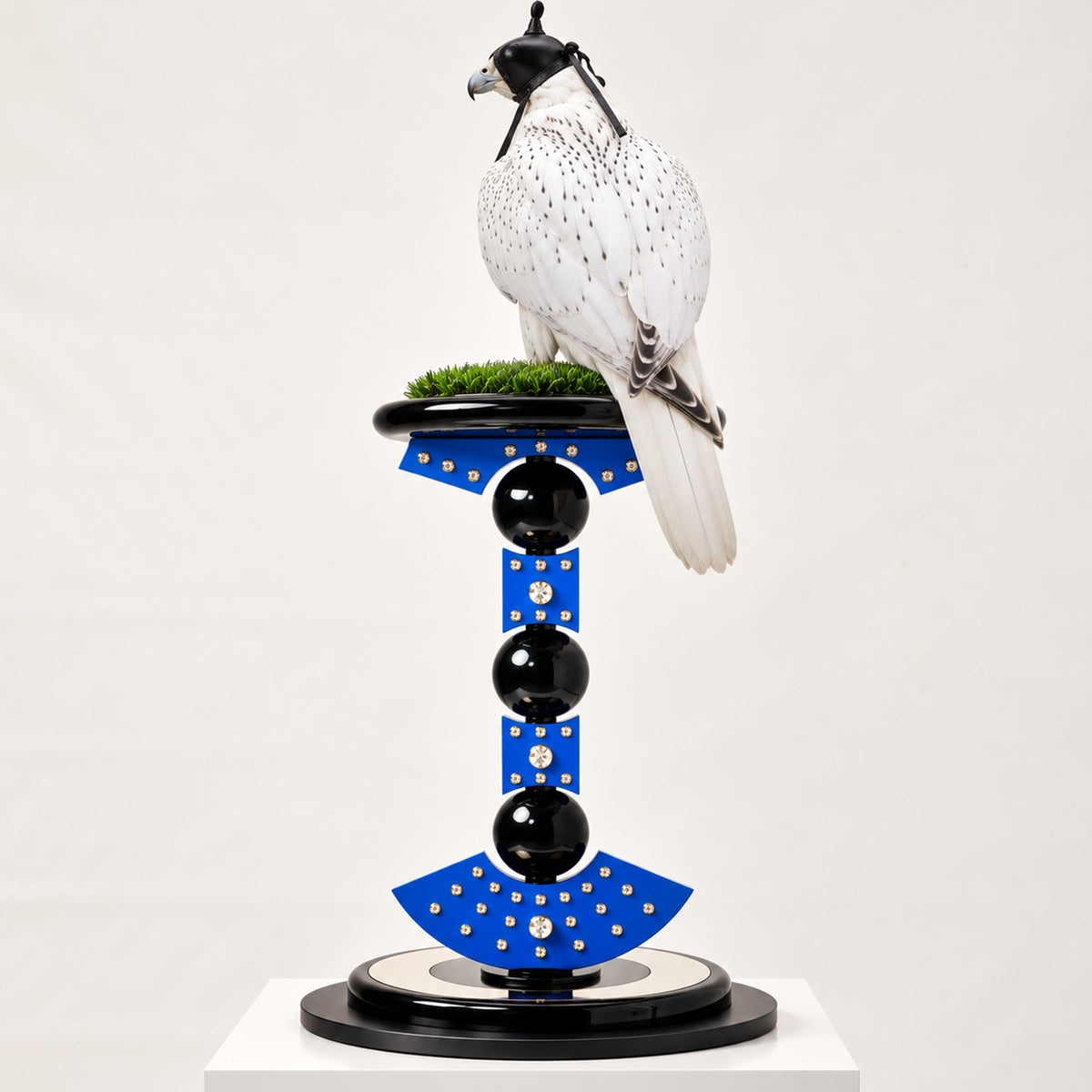 White hooded falcon perched on the FUROAR ZARINOR Imperial Falcon Perch, featuring vivid blue architectural panels, crystal detailing, glossy black spheres and a sculptural black circular base.