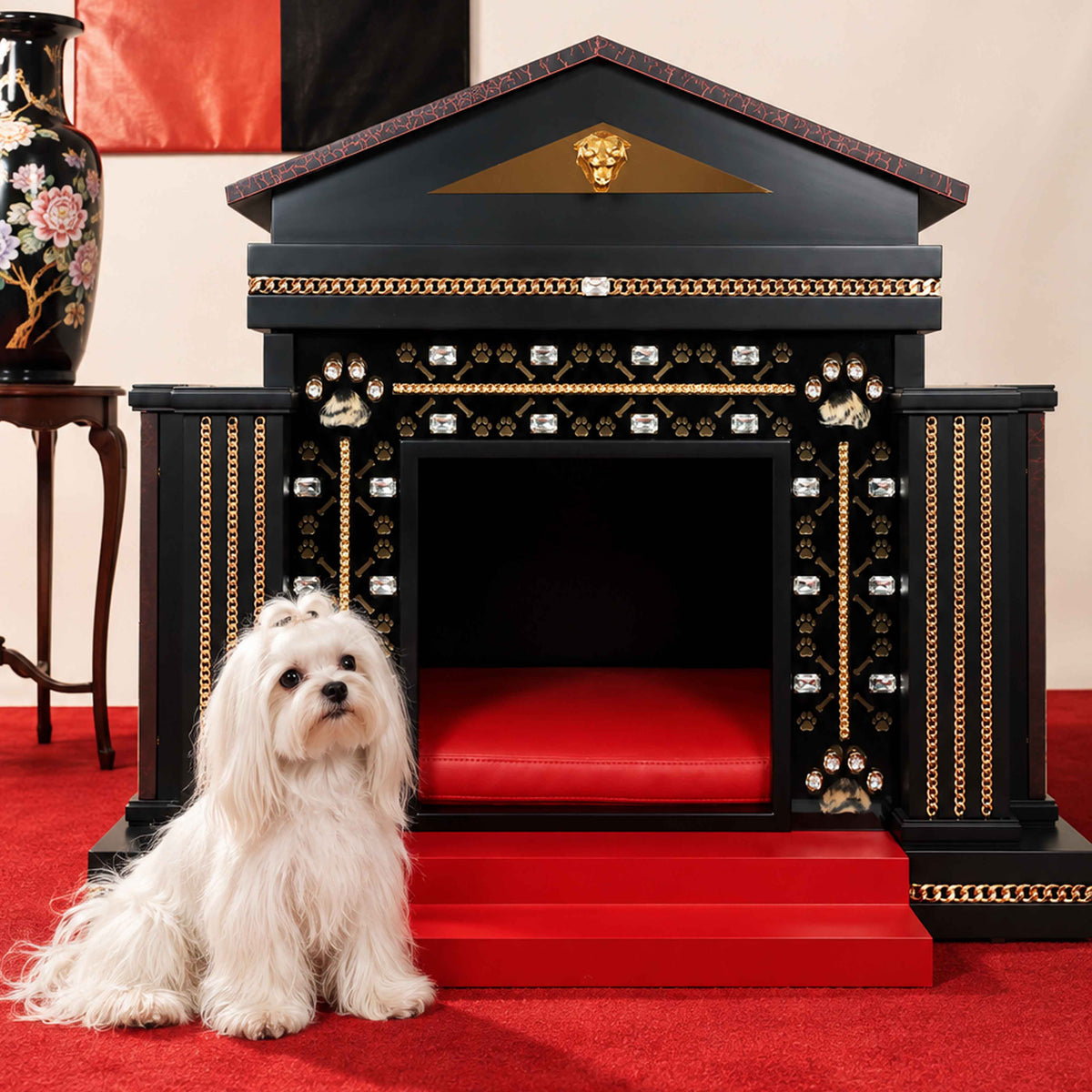 Photorealistic white Maltese dog sitting on a red carpet beside a black, red and gold FUROAR luxury dog kennel, featuring crystal embellishments, gold chain detailing, paw motifs, red entrance steps and a plush red interior.