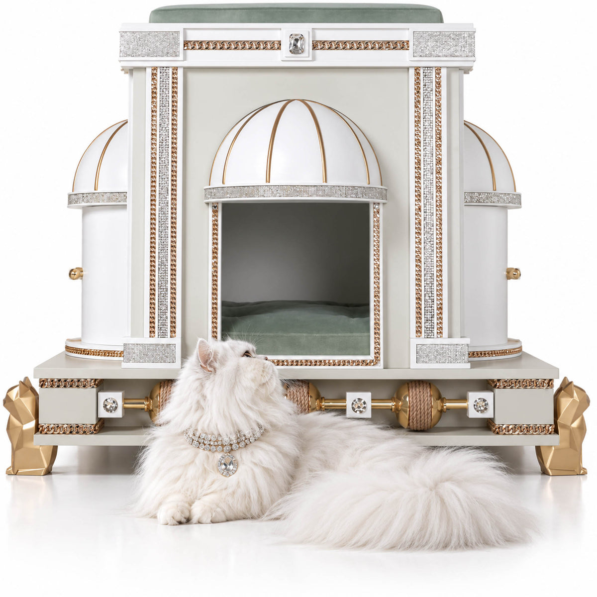 A fluffy white long-haired cat lies in front of an ornate white cat house with gold trim and domed entry, photographed on a clean white studio background.
